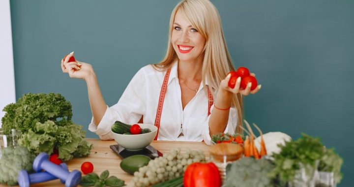 Healthy lifestyle concept with woman holding tomatoes and surrounded by fresh vegetables in a studio setting.